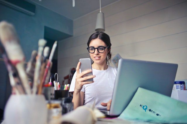 A young woman sitting in an art studio looking at her smartphone.