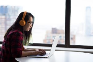 Millennial woman typing on laptop with headphones.